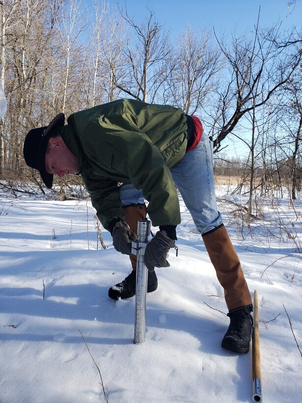 A man takes a snow sample with a snow tube.