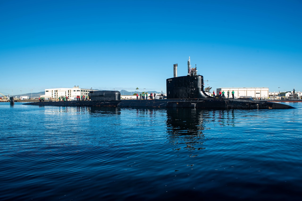 A submarine floats on the water’s surface in port.