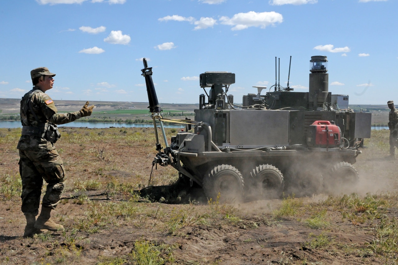 A soldier walks near a wheeled farm vehicle as it crosses a field.