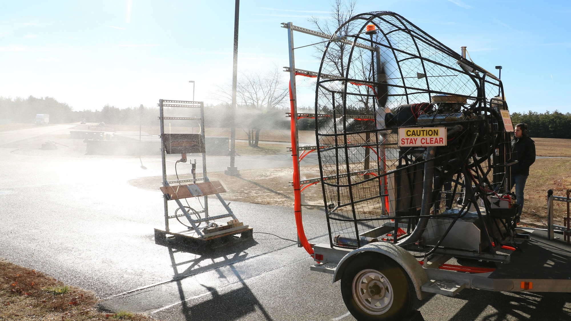 The Environmental Test Lab’s Blowing Rain Test Apparatus, outfitted with water tubing and placed on a moveable platform, simulates a blowing rainstorm during a test on a Hangar Structure and Outline Light and a Line-Up Light for USS Zumwalt. The fanboat can produce winds up to 110 miles per hour and 48 inches of rain.