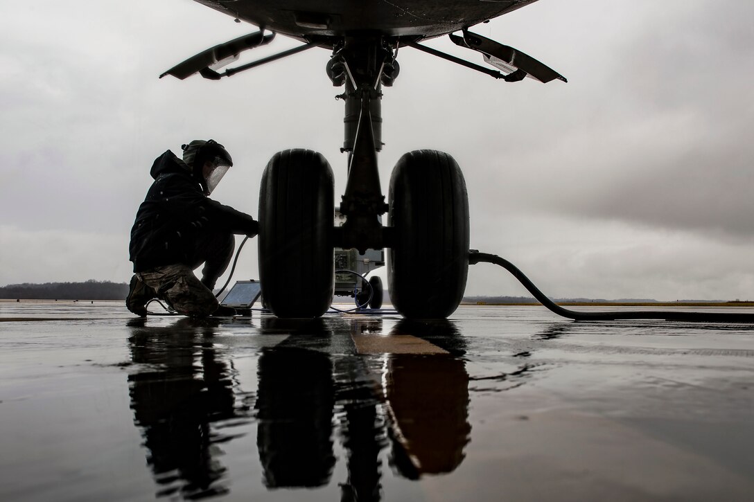 An airman kneels down to service a tire on an aircraft.