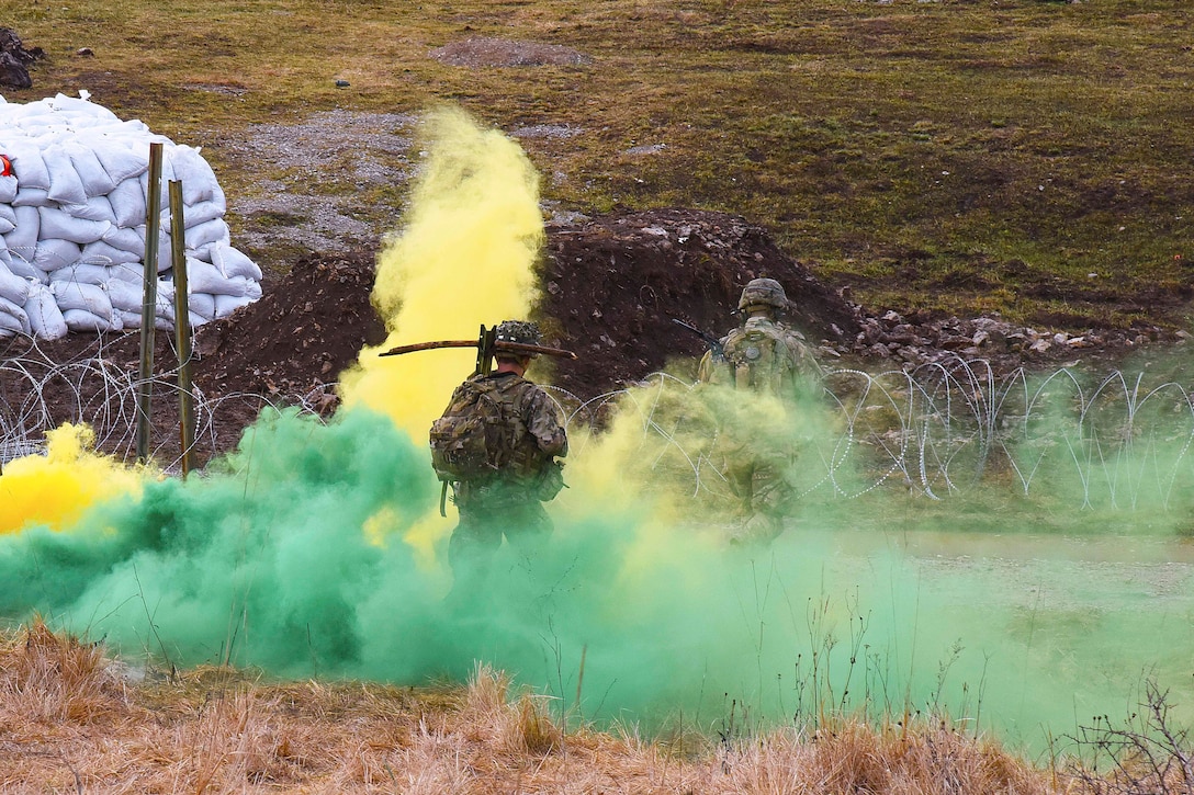 Soldiers in uniform stand in a field surrounded by green and yellow smoke.