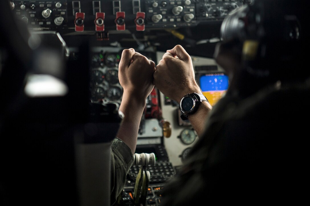 Two airmen fist-bump in the cockpit of an aircraft.