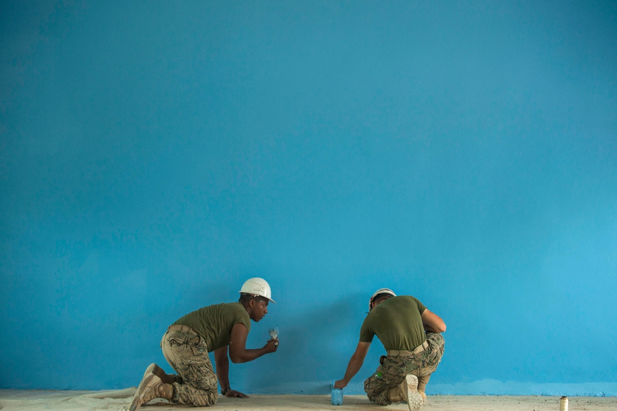 Two Marines paint a wall turquoise blue.
