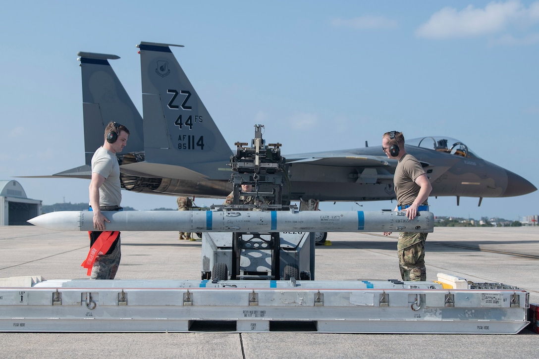 Two airmen lift a missile and prepare to load it on a military aircraft.