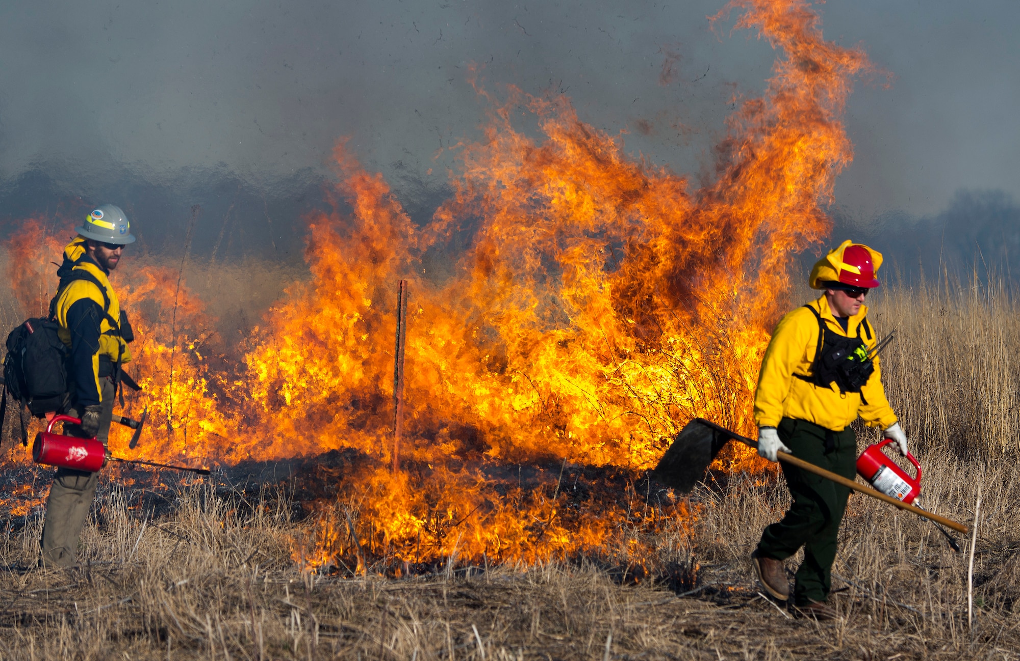 Nick Steel, Air Force Wildland Fire Branch Wildland Support Module, and District Chief Matt Dickey, Wright-Patterson Air Force Base, Ohio, Fire Department, part of the 788th Civil Engineer Squadron, walk with drip torches Feb. 21, 2020, helping to spread a prescribed burn on Huffman Prairie. The two units combined in an effort to manage the fuel on the prairie and help the prairie grass grow. (U.S. Air Force photo/R.J. Oriez)