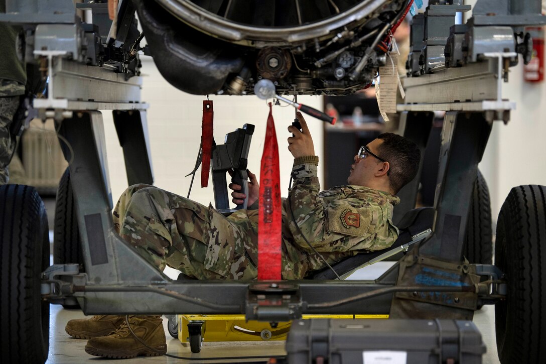 An airman lays underneath of a jet’s engine to inspect it.