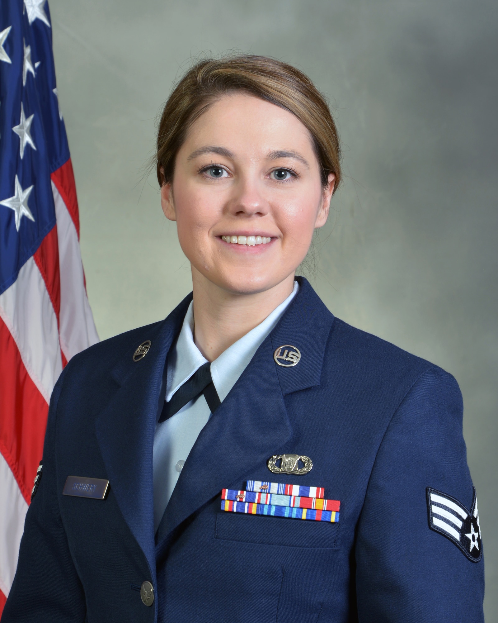 head and shoulders of military woman in uniform, gray background and U.S. flag over her right shoulder