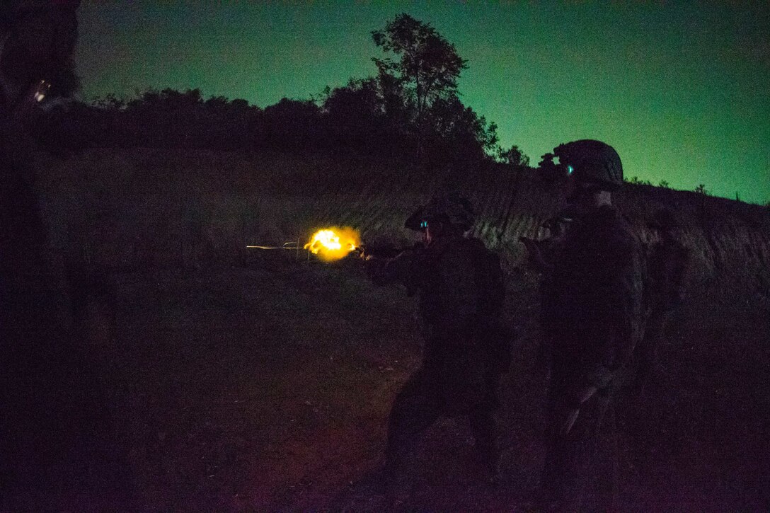 A Marine fires a weapon in a field illuminated by a green light.