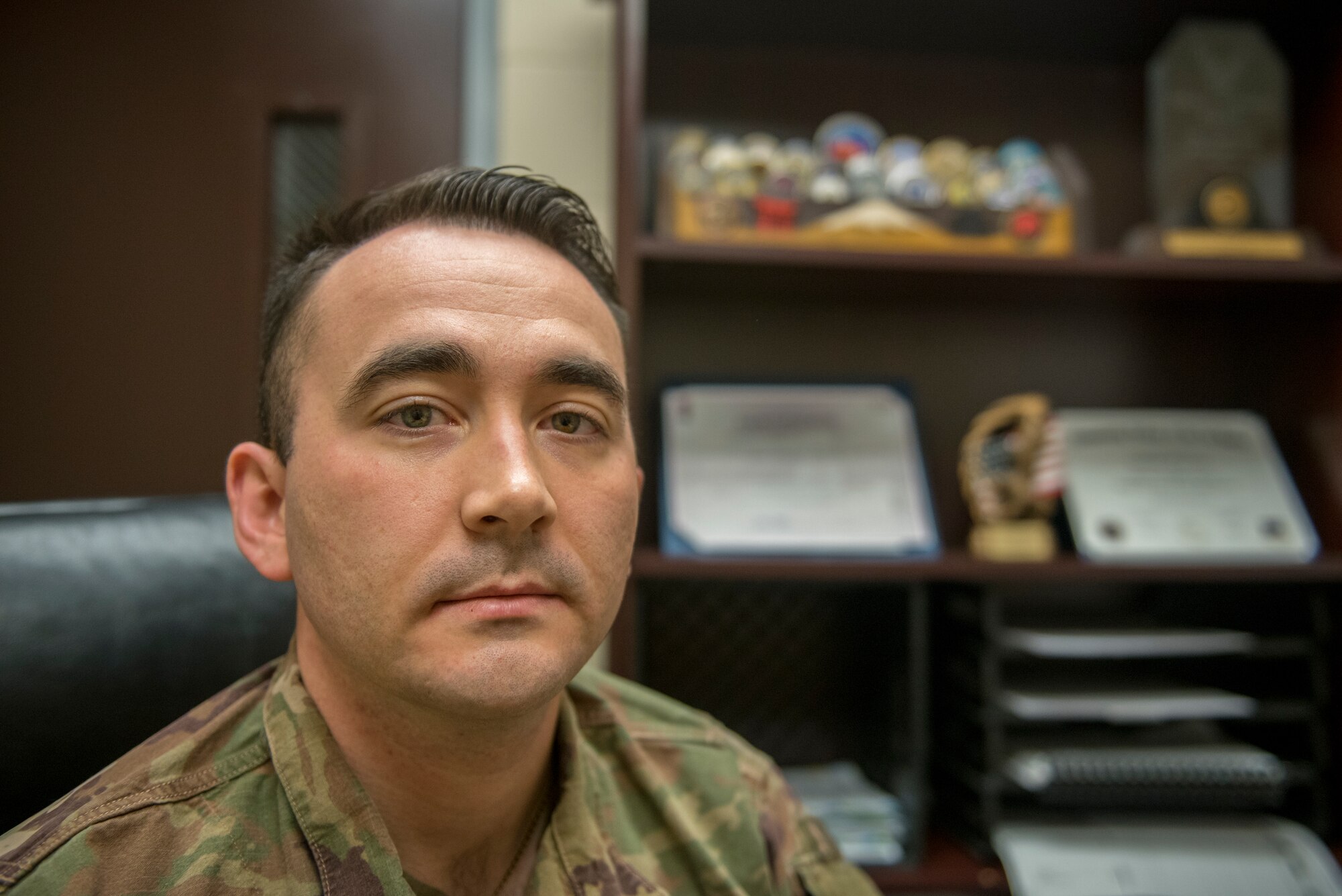 Man sits in room with awards and other accolades behind his left shoulder.