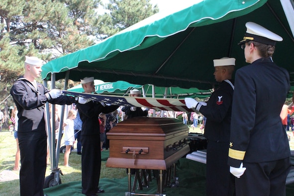 A woman in uniform salutes the flag held over a casket by navy personnel at a funeral.