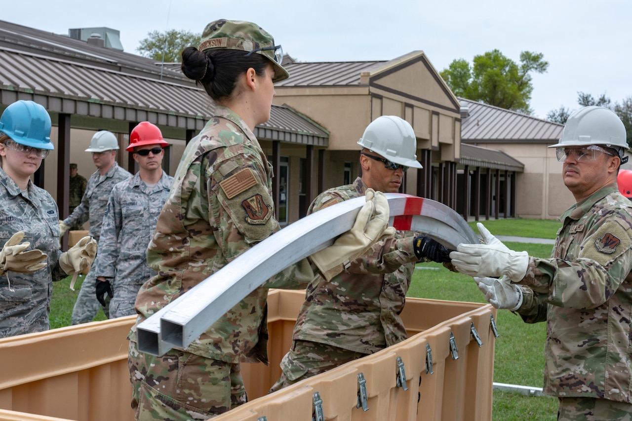 Airmen lift metal rods out of a large wooden box.