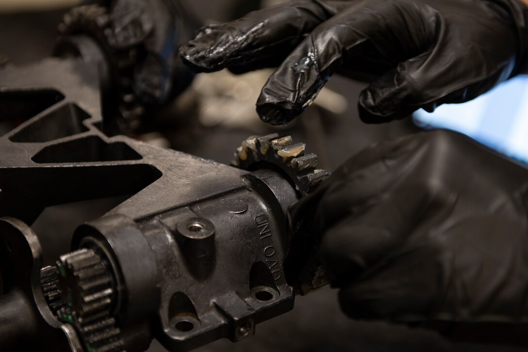 A photo of an Airman applying aircraft grease to a transfer unit gear.