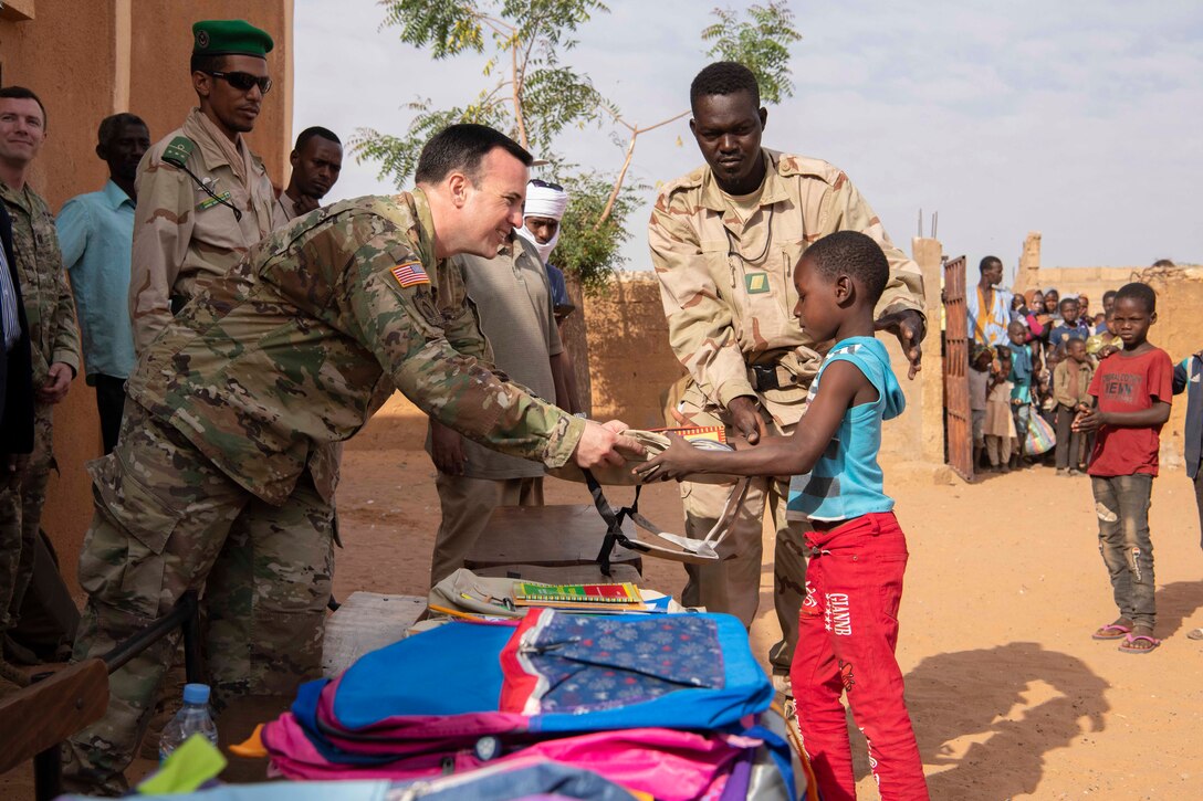 A soldier hands a notebook to a child; others surround.