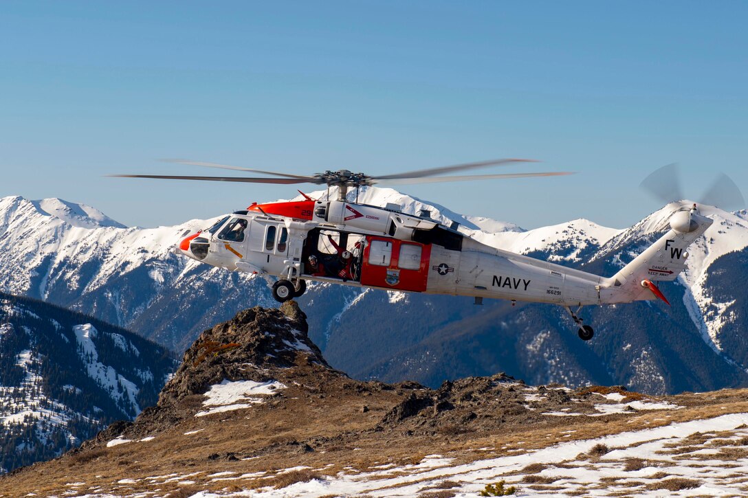 A Navy helicopter prepares to land on a snowy mountain.