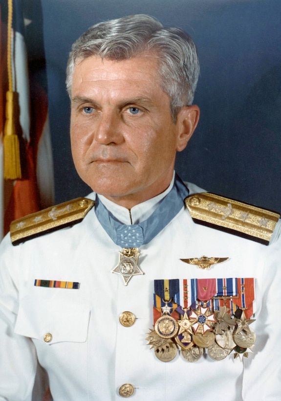 A man with gray hair sits for an official photo wearing a military uniform, a slew of medals on his chest and a Medal of Honor around his neck.