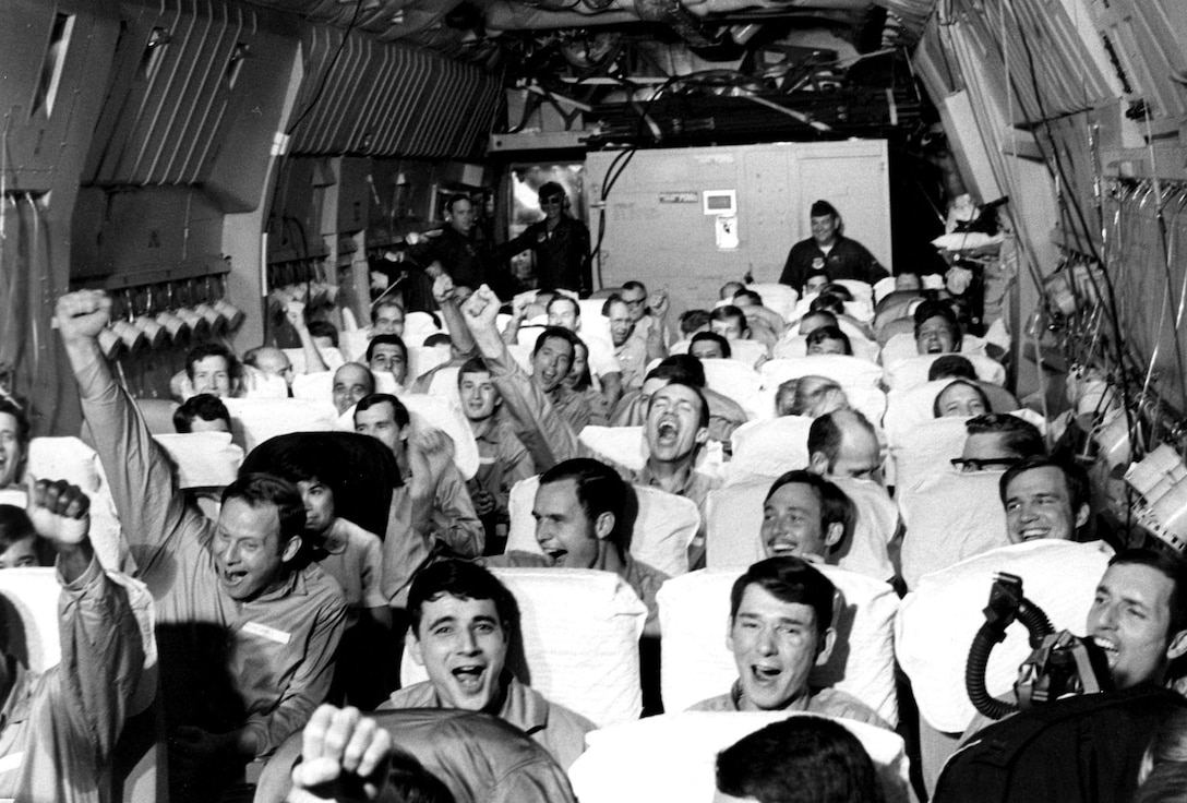 A cargo airplane is packed with men, who are smiling and cheering with their hands raised.