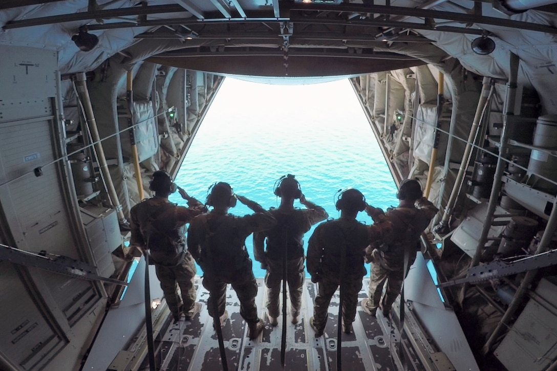 Airmen in uniform salute while standing in the opening of an aircraft.