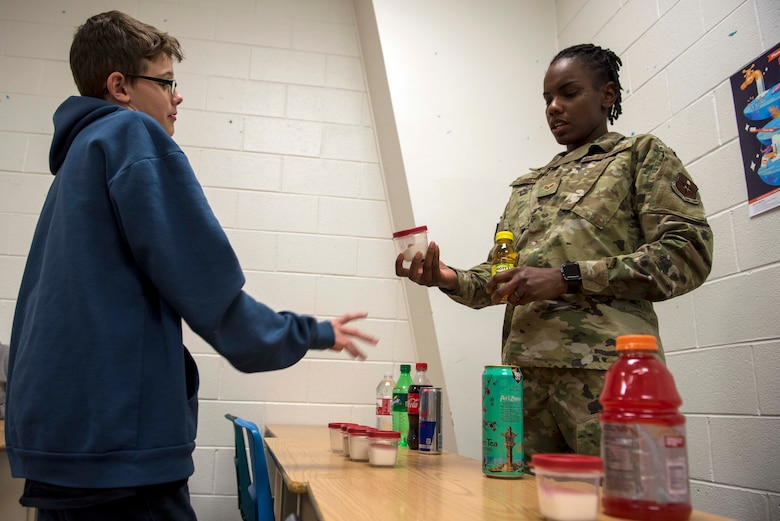 Senior Airman Juanita Black, 49th Operational Readiness Medical Squadron Dental Flight technician, explains the amount of sugar found in sugary drinks, Feb. 26, 2020, at Holloman Middle School on Holloman Air Force Base, N.M. On an annual-basis, the dental flight visits the Holloman Child Development Center, Holloman Elementary School and Holloman Middle School, providing them with knowledge on proper brushing techniques and the negative effects of not brushing teeth. (U.S. Air Force photo by Staff Sgt. Christine Groening)