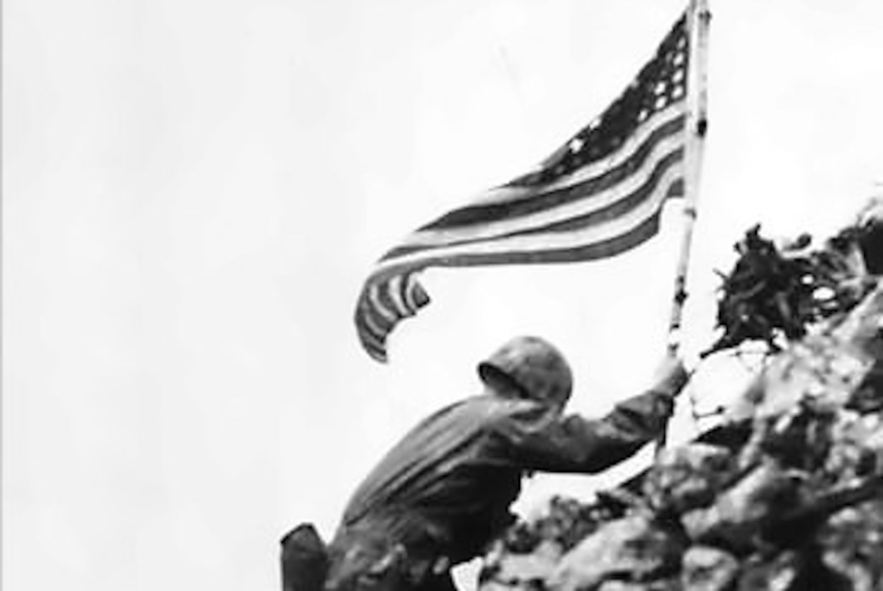 Man carries flag up rocky slope.