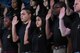 Nine young men and women of different races in black t-shirts raise their right hands.