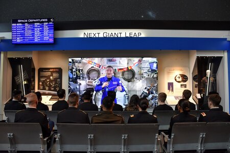 rows of people sitting in chairs watching a man in space on a large sized display.