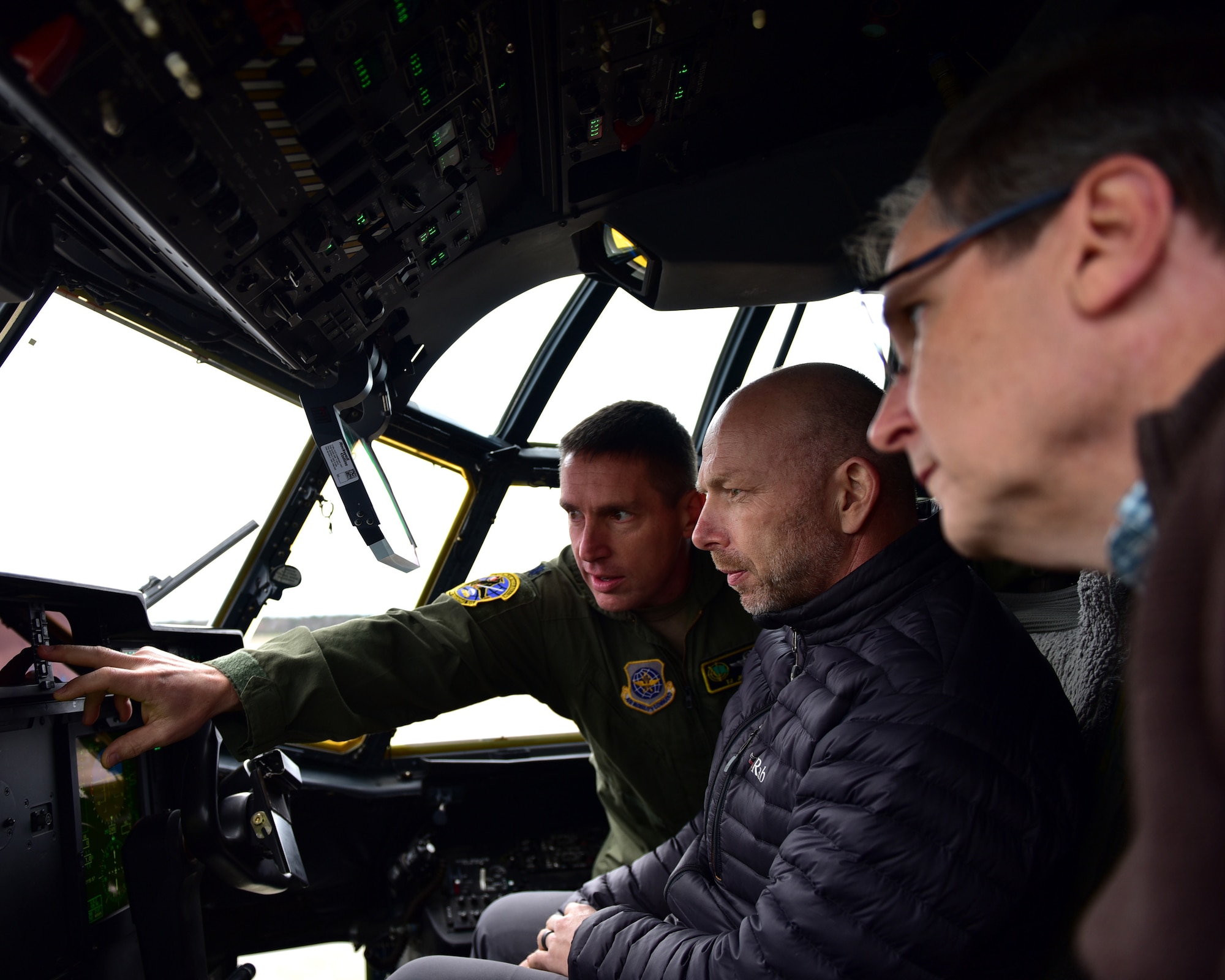 three people sit in the flight deck of a C-130J