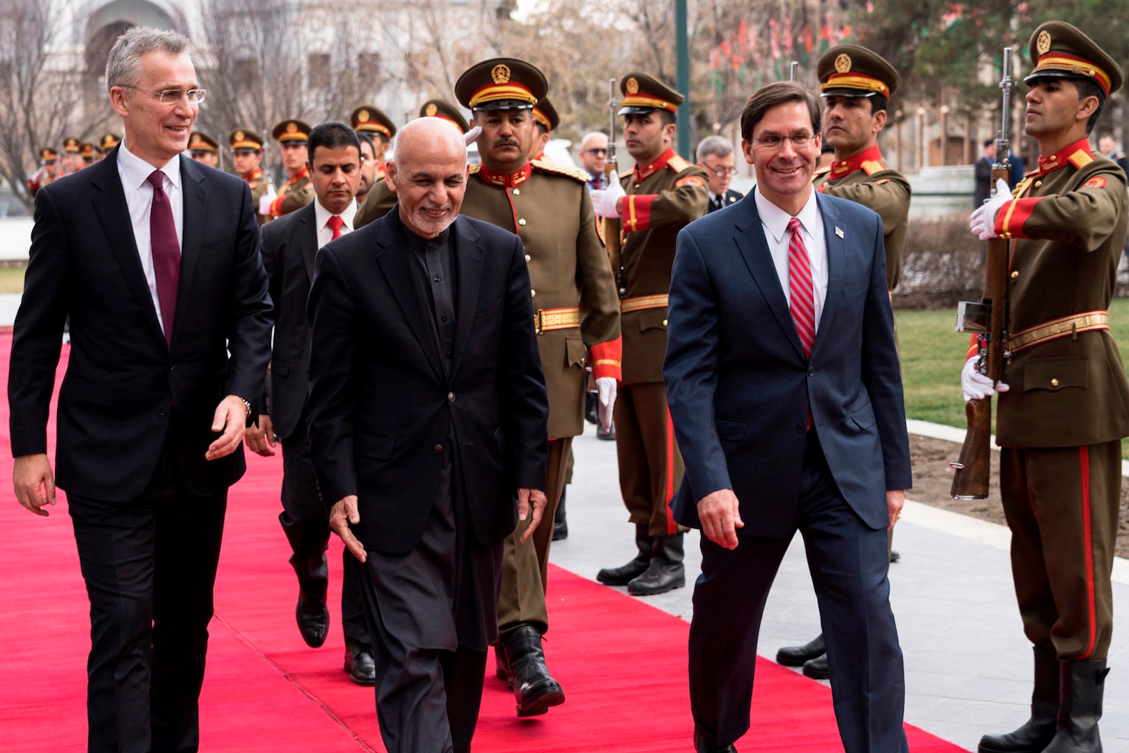 Defense Secretary Dr. Mark T. Esper and two other civilians walk on a red carpet.