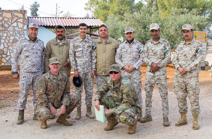 Group of 9 US and Jordanian Soldiers standing together, posing for photo.