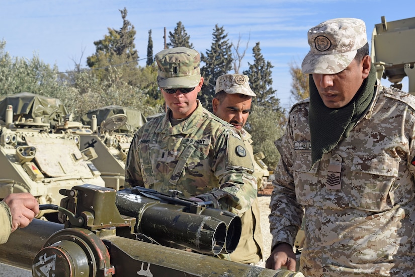 Three US and Jordanian Soldiers observe BGM-71 Weapon System outdoors while another Soldier operates a lever