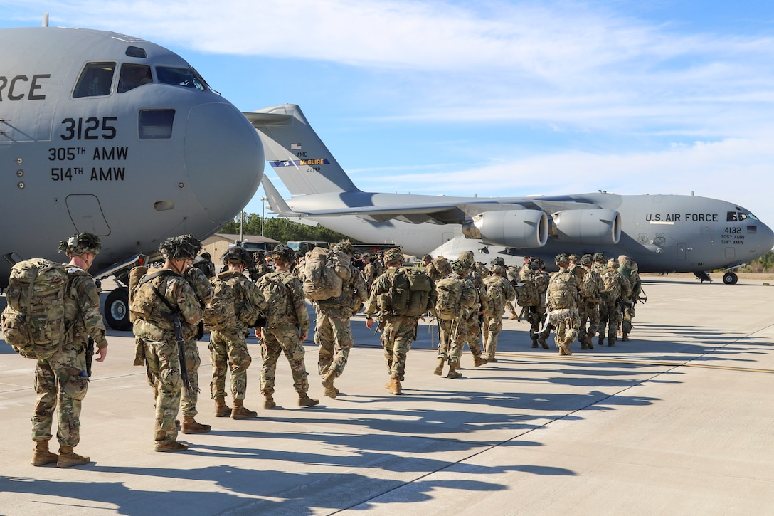 A long line of soldiers walks toward an aircraft on a flightline.