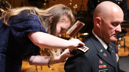 The daughter of Warrant Officer 4 Jonathan D. Ward, commander and band master of “Fort Sam’s Own” 323rd U.S. Army Band, places shoulder boards with his new rank during his promotion to Chief Warrant 5, at the University of the Incarnate Word’s Luella Bennack Concert Hall in San Antonio Dec. 3, 2019.