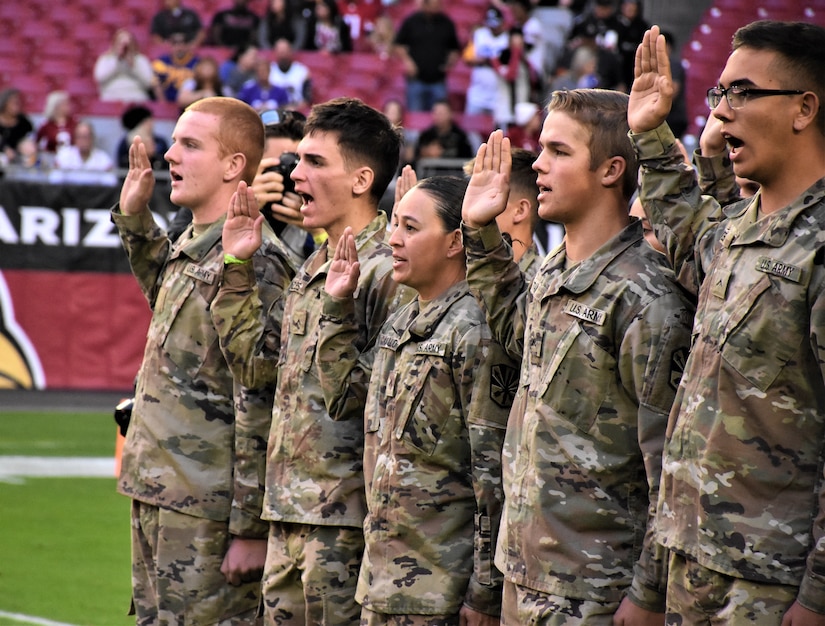group of men and women in Army uniforms hold up their right hands and take the oath of enlistment.