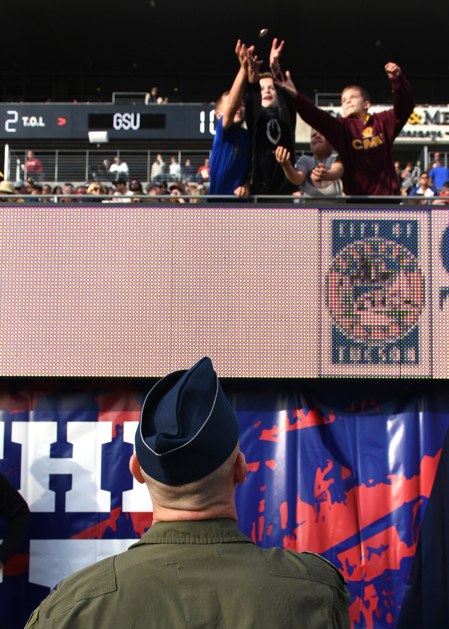 Photo of a servicemember throwing a challenge coin to young fans at a football game