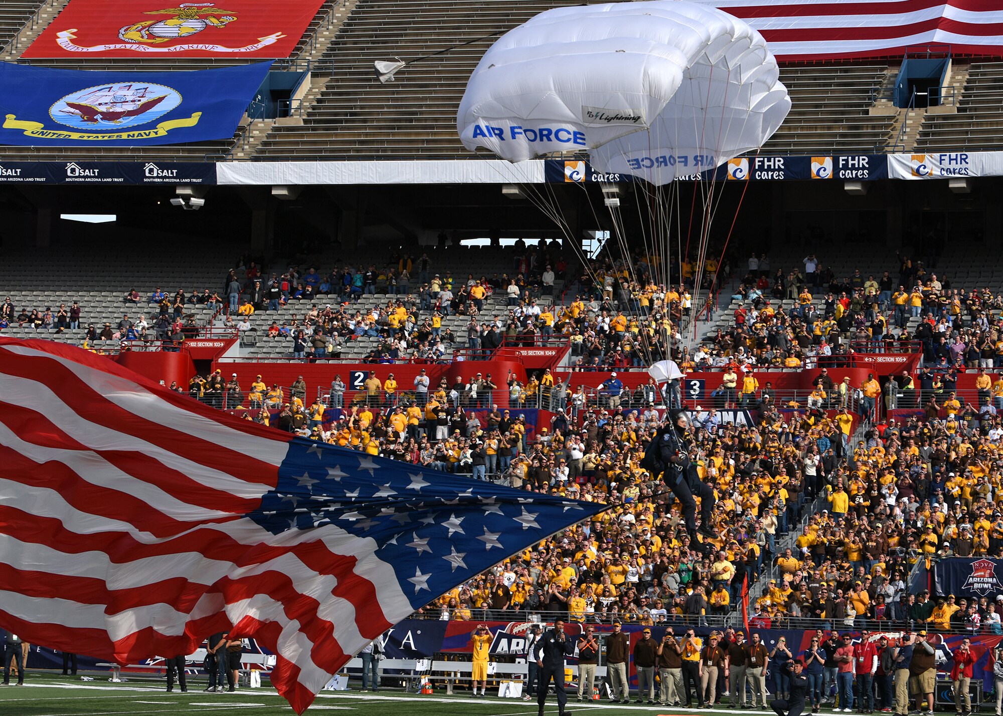 Photo of a U.S. Air Force skydiving team member parachuting with a U.S. flag onto a football field