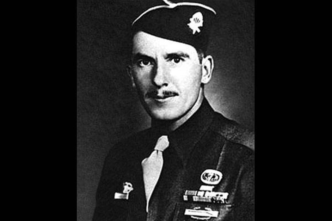 A soldier in dress cap and jacket with ribbons poses for an official photo.