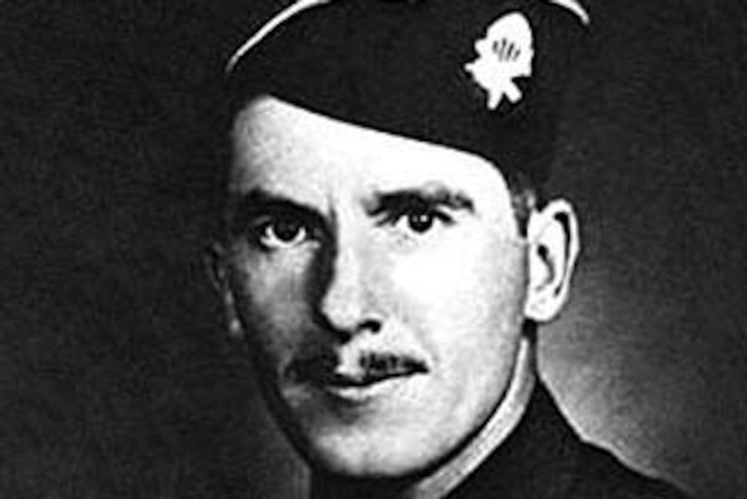 A soldier in dress cap and jacket with ribbons poses for an official photo.