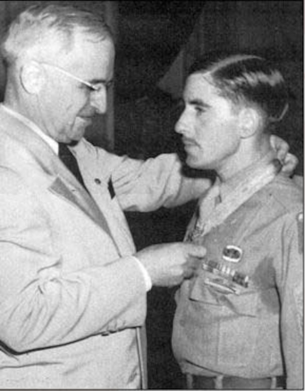 President Harry S. Truman places the Medal of Honor around the neck of a soldier who stands at attention.