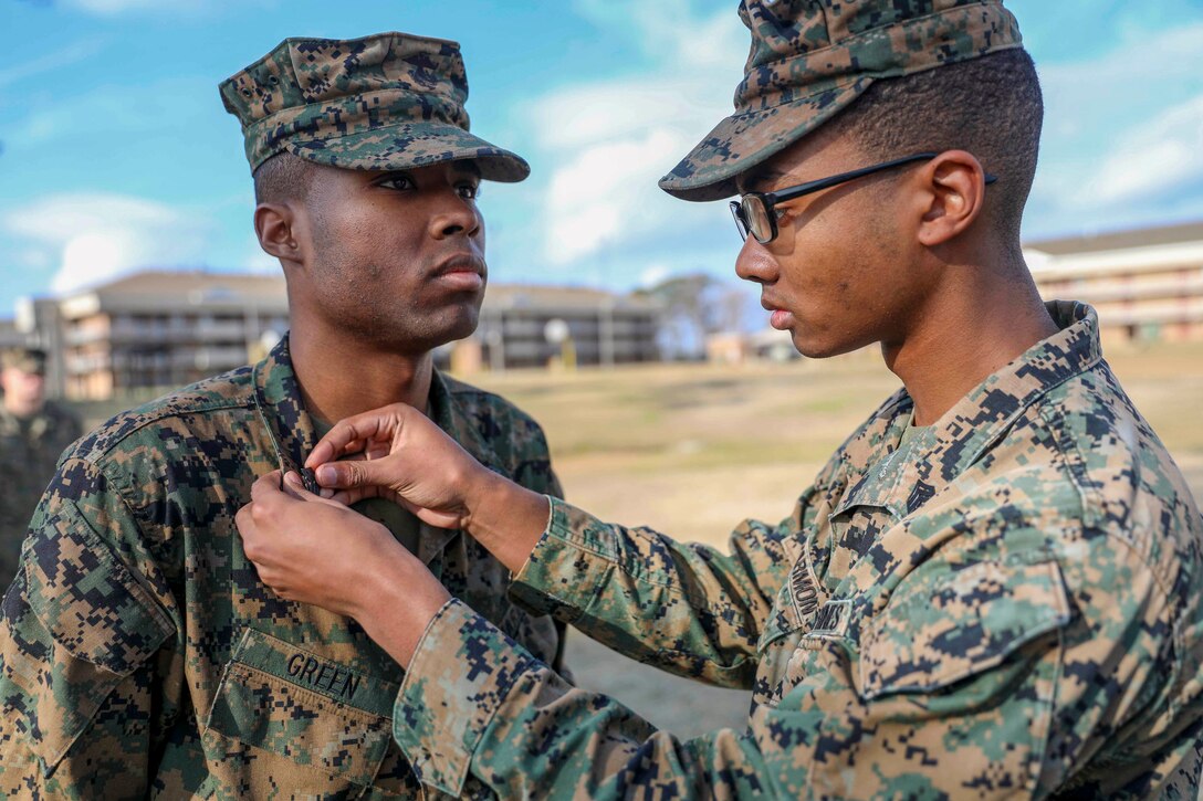 A Marine affixes a pin to another Marine's collar outside near buildings.