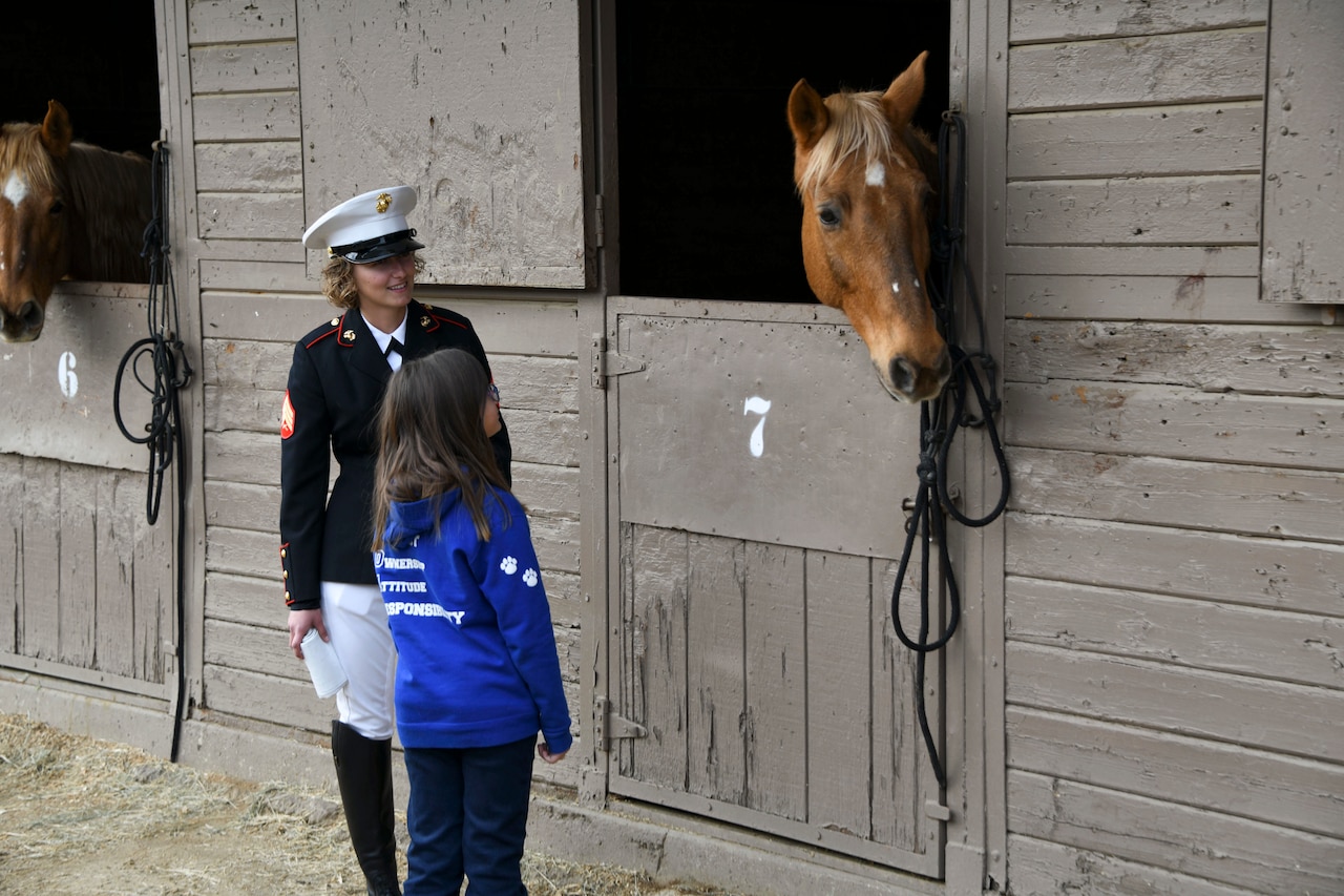 A Marine speaks to a child outside a stable as a horse is peers out.