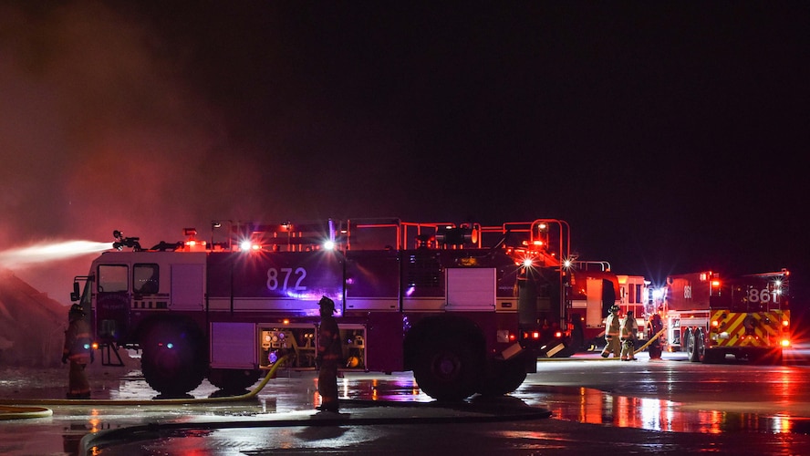 Firefighters spray water onto the burning hangar Dec. 28, 2019, at Minot Air Force Base, North Dakota. The fire trucks pressurize water to extinguish the flames. (U.S. Air Force Photos By Airman 1st Class Caleb S. Kimmell)