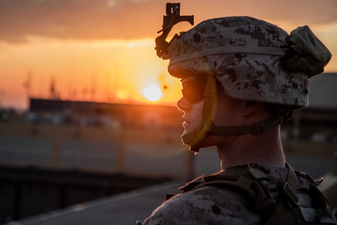 A Marine stands watch at his post with the sun behind him.