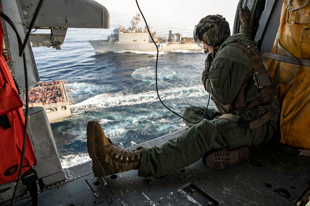 A sailor aboard an open aircraft looks out over two ships in the ocean.