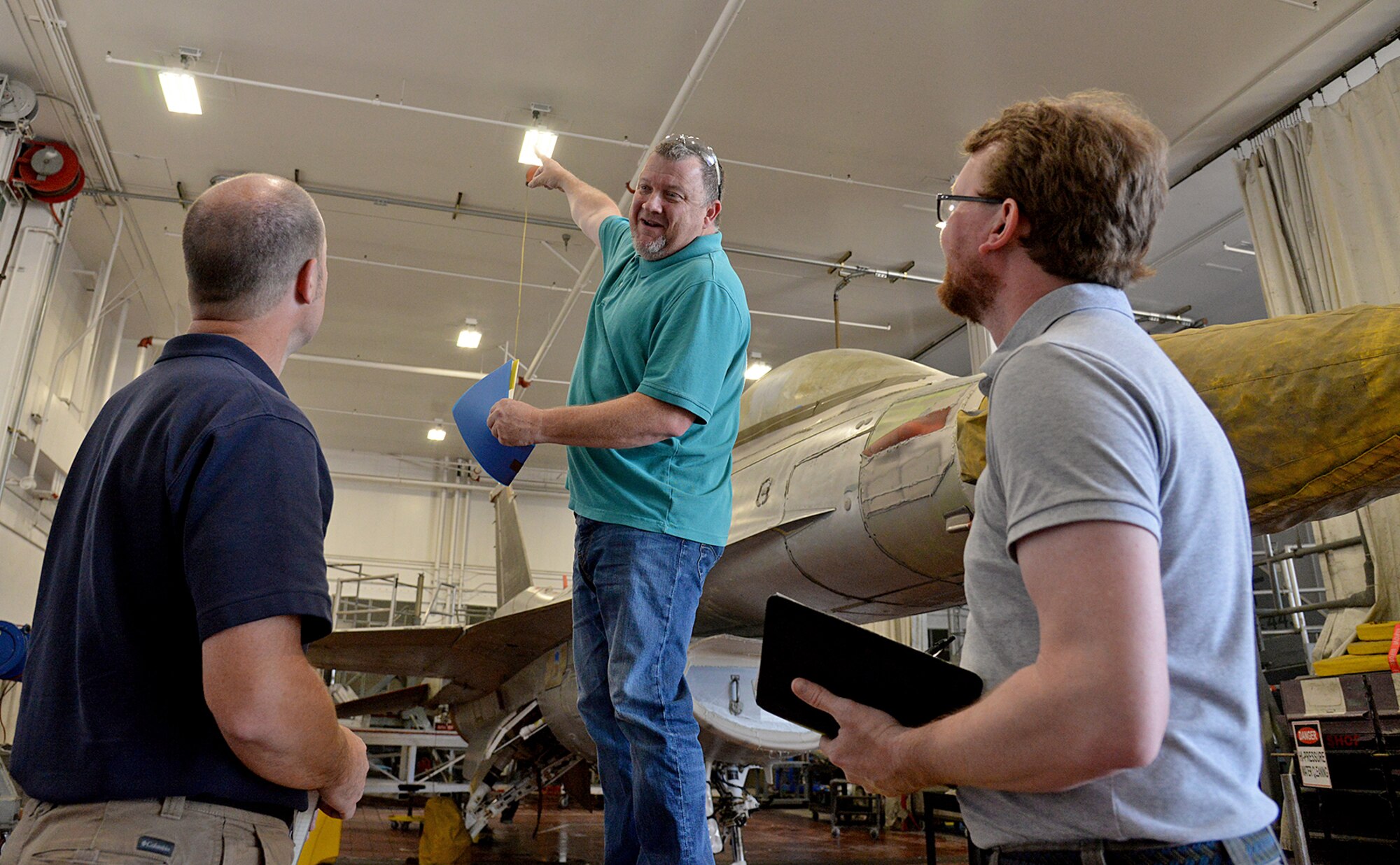 Shane Jepson, facility manager for building 220, points at new energy saving light fixtures on the ceiling in a depot maintenance facility to auditors Rob Ellis (left) and Jonathan Clark