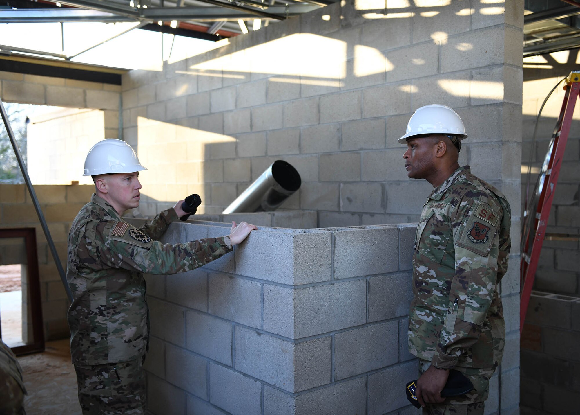 An Airman talks to another Airman in a building that is under construction.