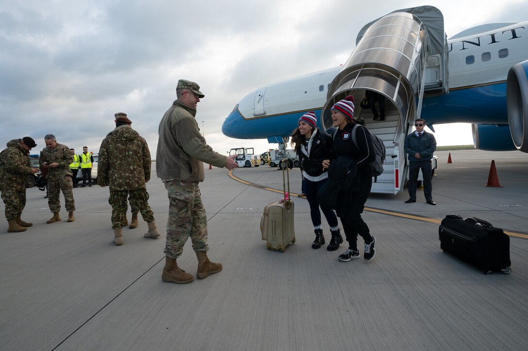 Service members in uniform greet USO Tour participants as they file off their airplane.