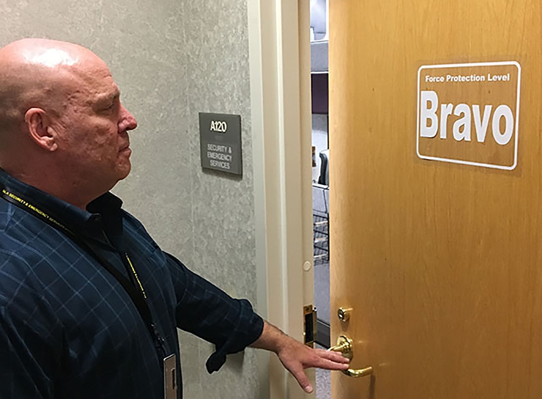 Man stands in front of office door with sign indicating the force protection condition is Bravo.
