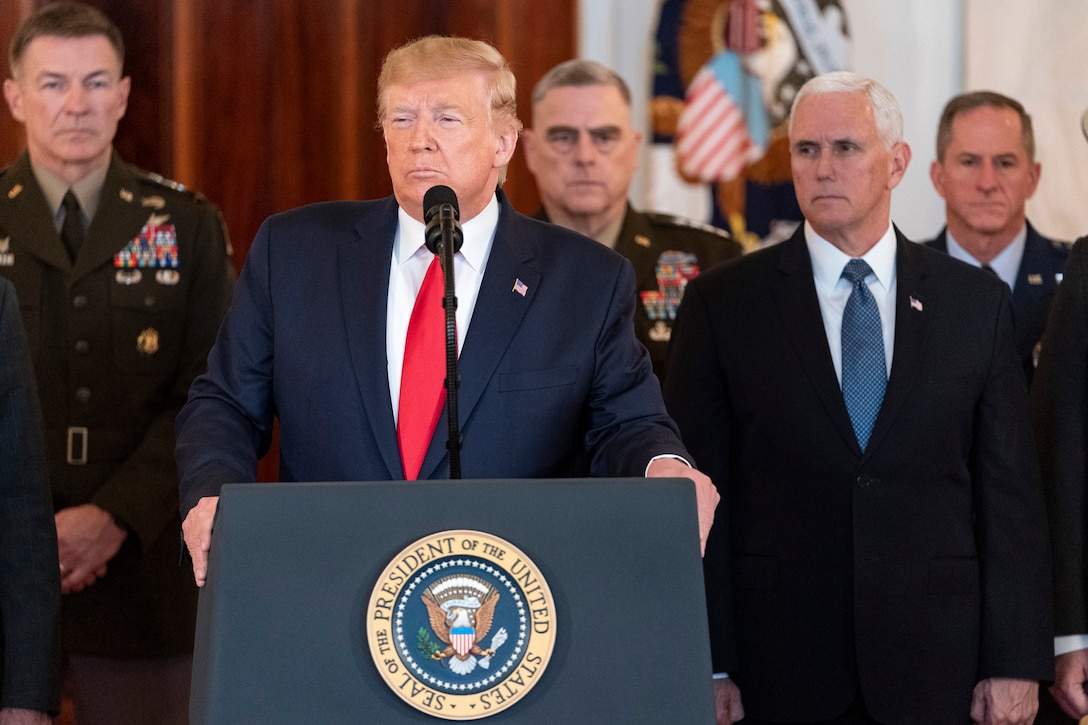 President Donald J. Trump stands at a podium speaking to the press, with senior advisors standing behind him.