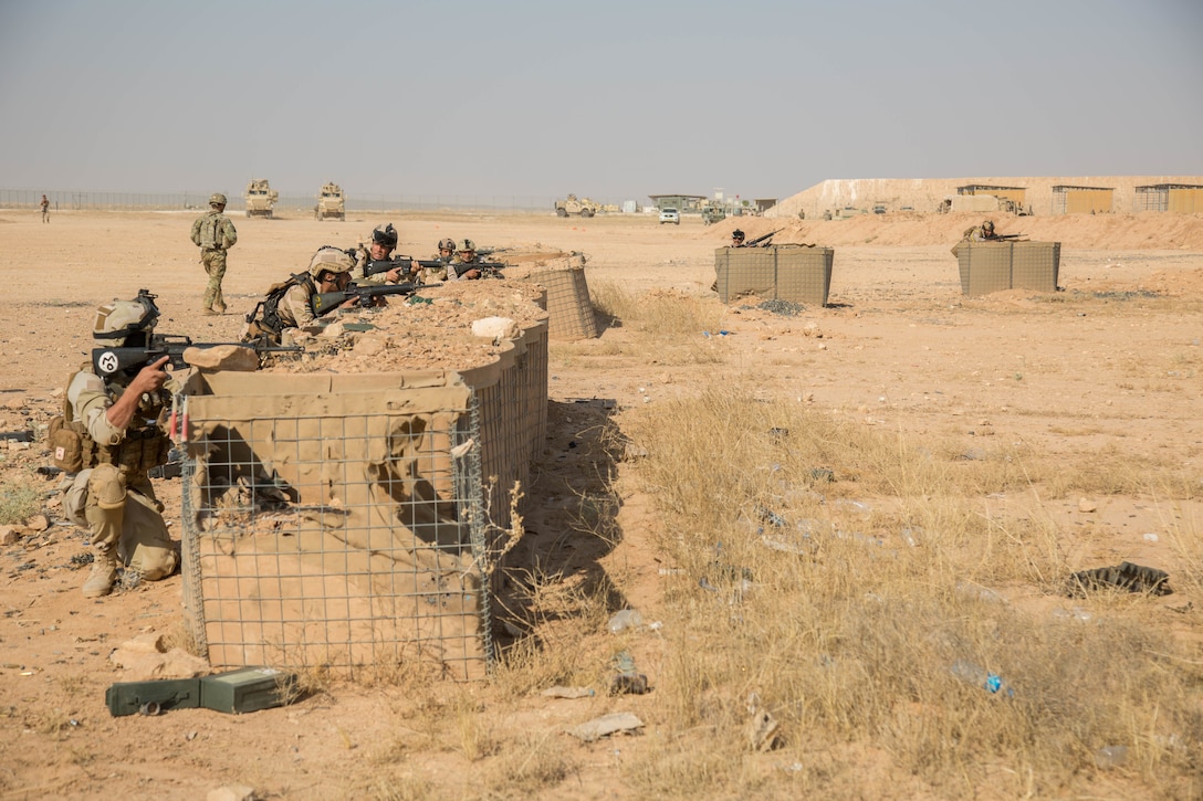 Soldiers in a desert setting fire weapons from behind barricades.