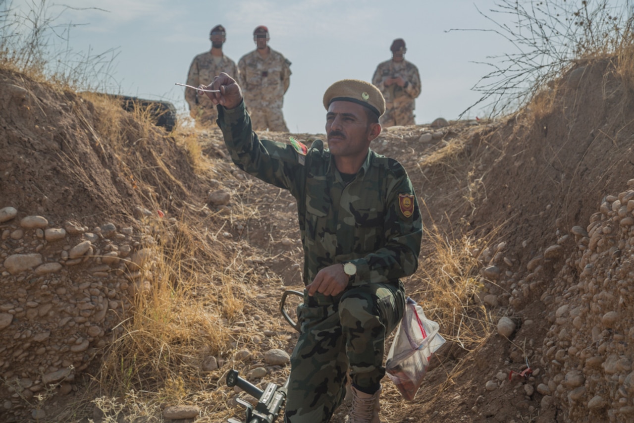 A soldier kneels to touch a trip wire.